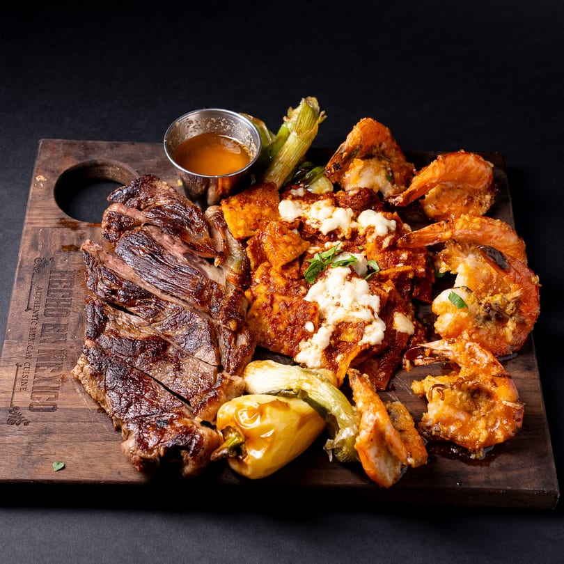 Hecho en Mexico's grilled steak, shrimp, chilaquiles, and vegetables on a wooden board.