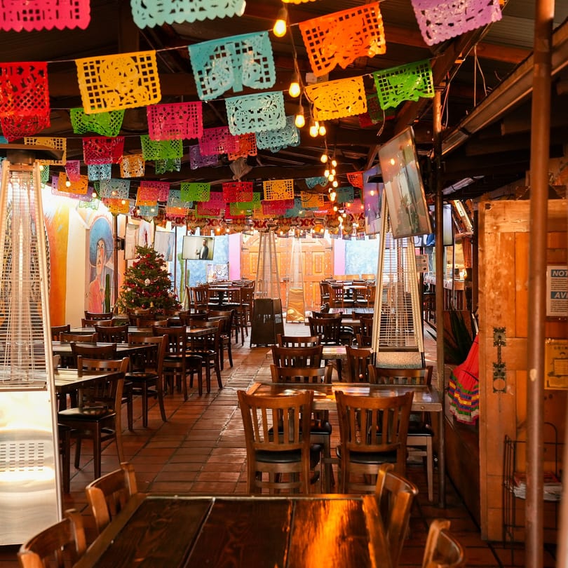 Hecho en Mexico restaurant interior with colorful papel picado, wooden tables, chairs, and a Christmas tree.